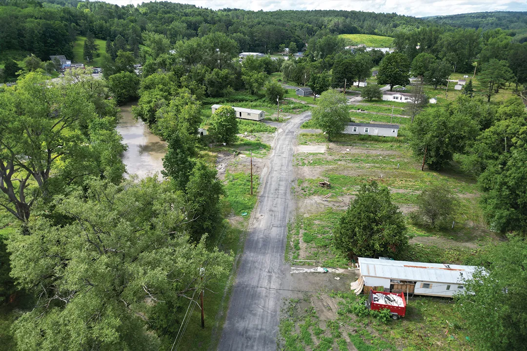 a vermont landscape featuring a river, dirt road, and three mobile home units