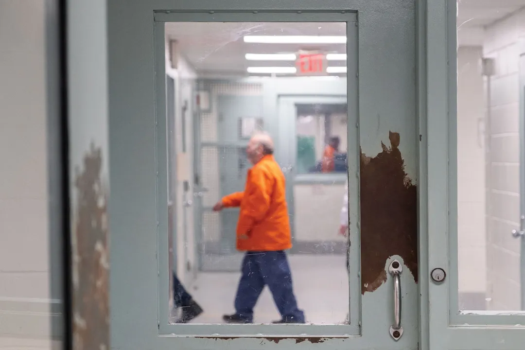 the sillouette of a person in an orange prison jumpsuit through the window of a prison security door