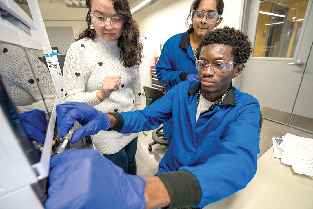 three scientists work in a lab looking at a microscope
