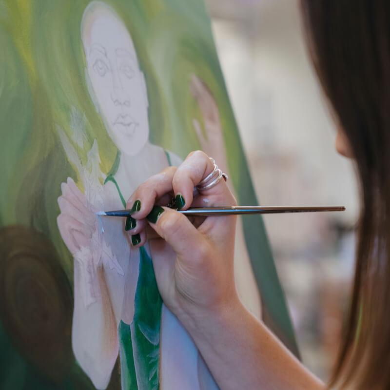 Closeup of a hand painting a person on canvas.