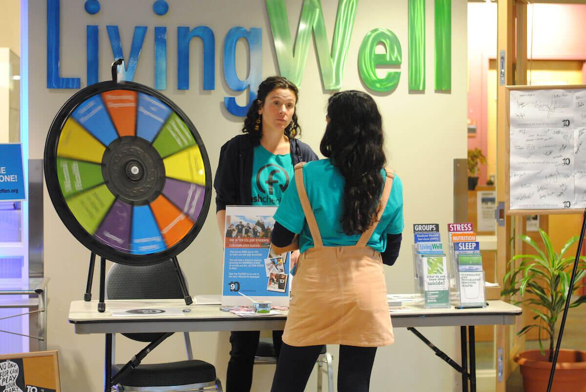 A woman stands at a booth in front of a sign reading 'Living Well'