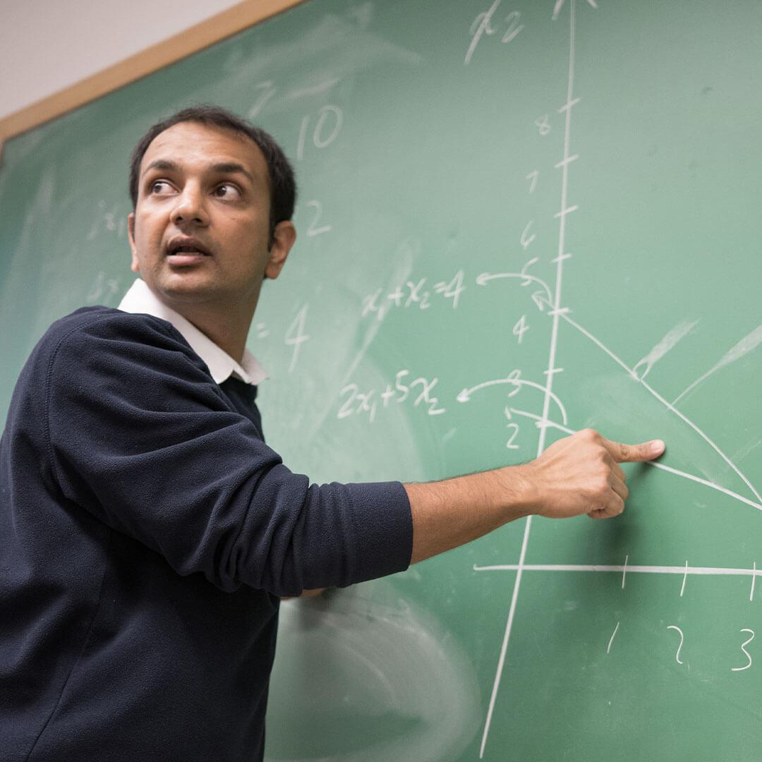 a professor points at an equation on a chalkboard