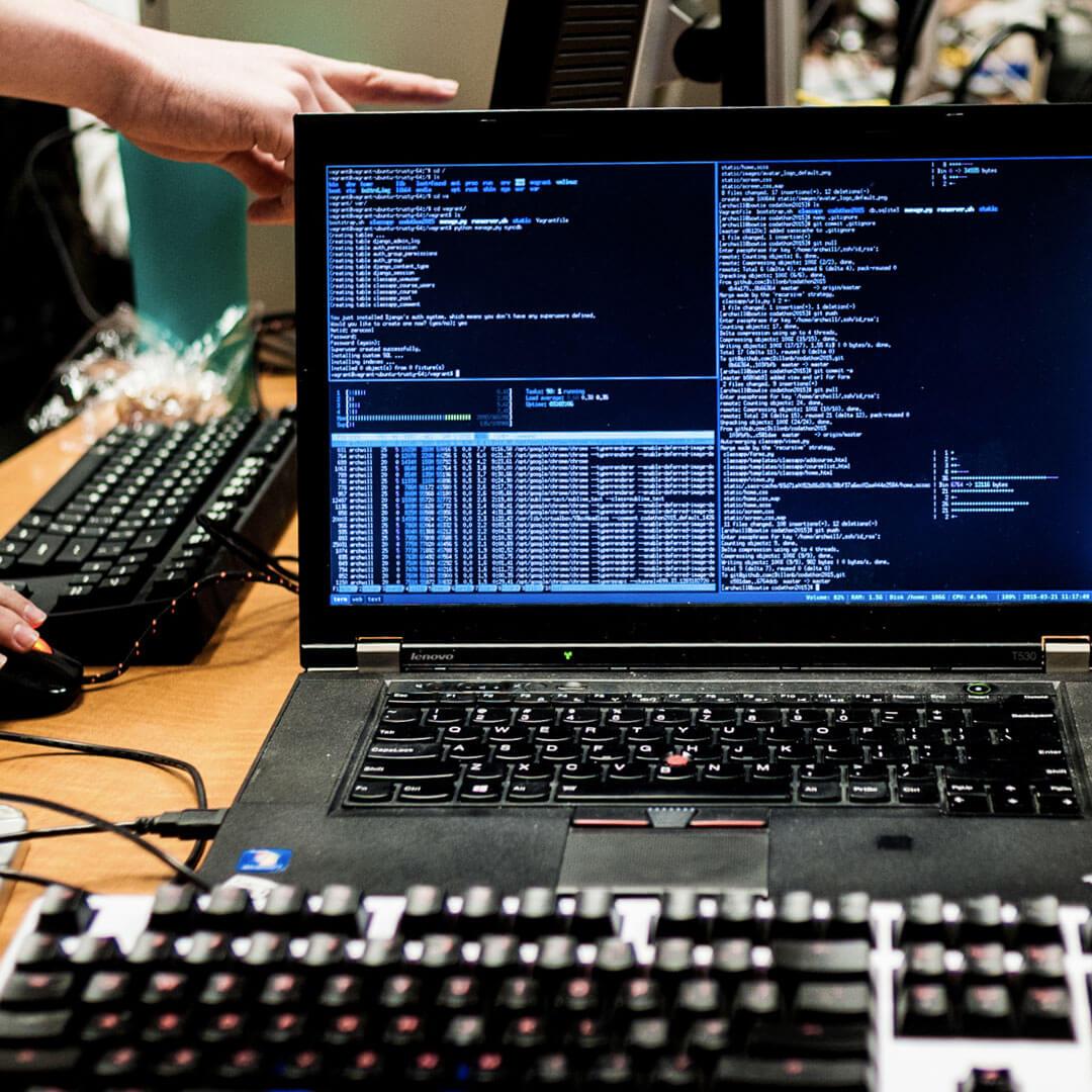 a hand points at a computer with code on the screen