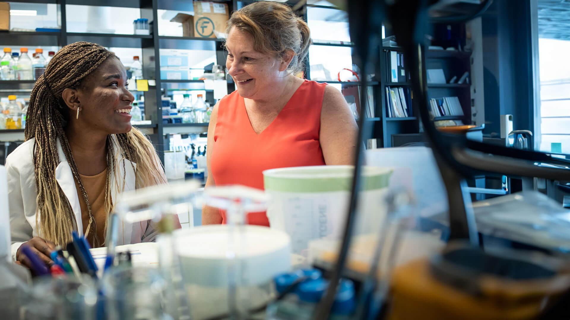 two individuals talking at a lab bench with beakers in the foreground