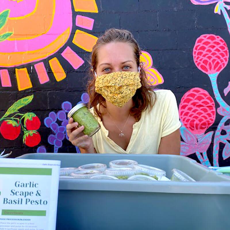 a student wearing a mask holds a jar of garlic scape and basil pesto