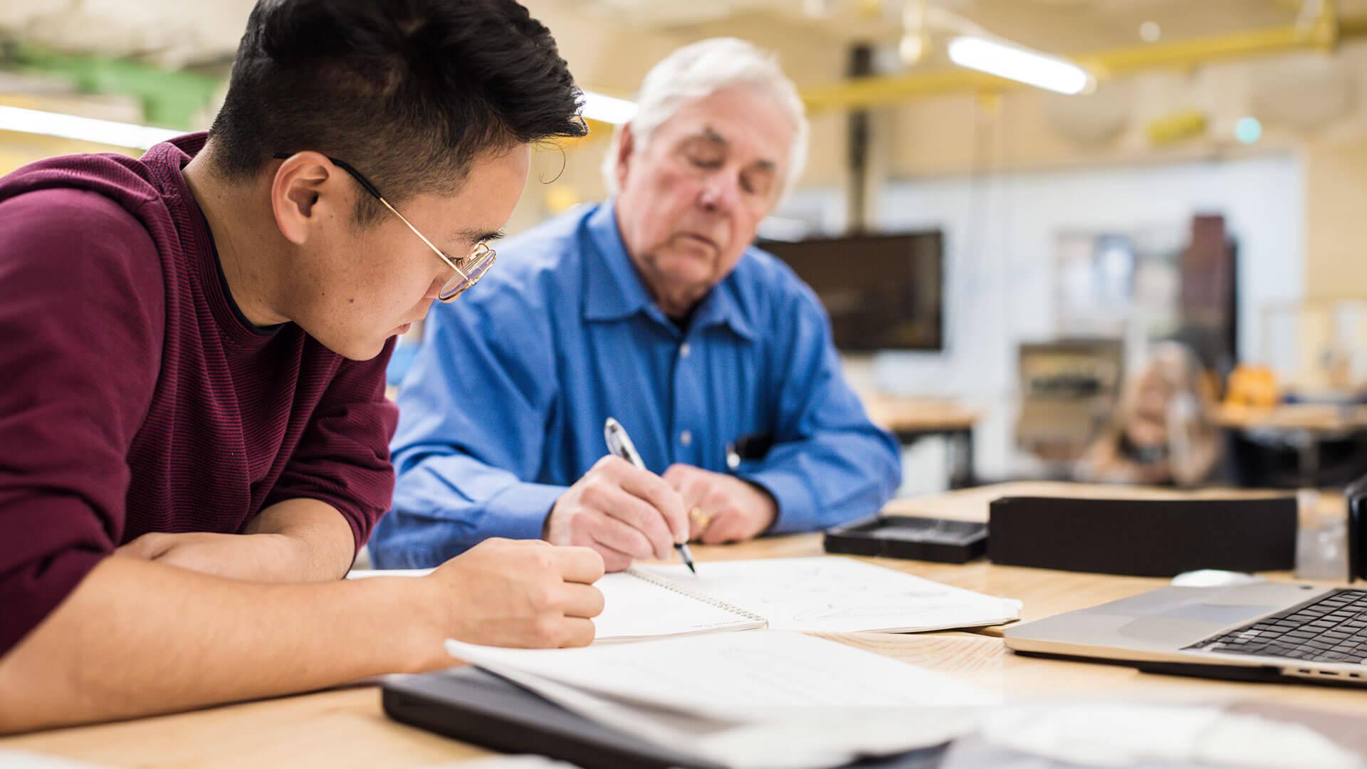 A student and advisor look at a notebook together.