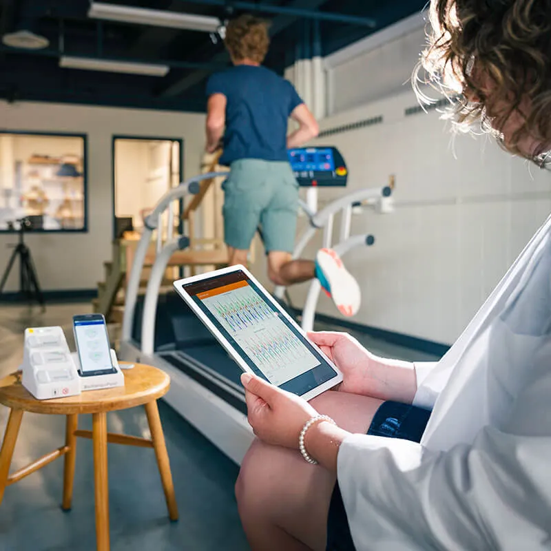 a person holds a ipad with data on it as another person with sensors on them runs on a treadmill