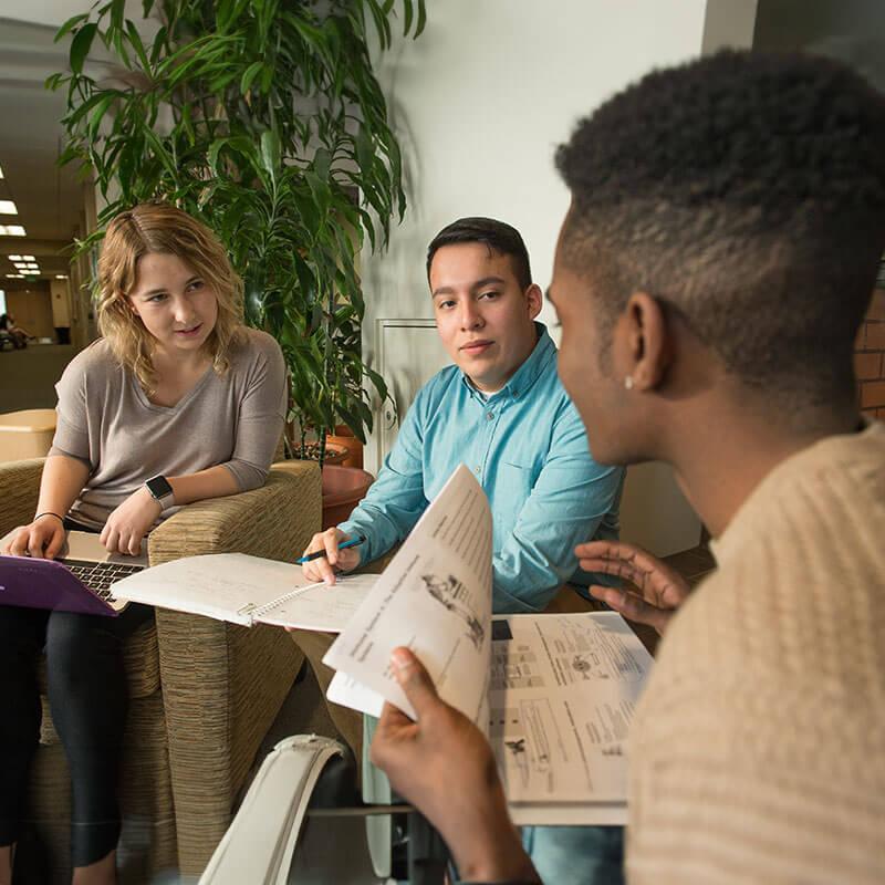 three students talk while flipping through materials