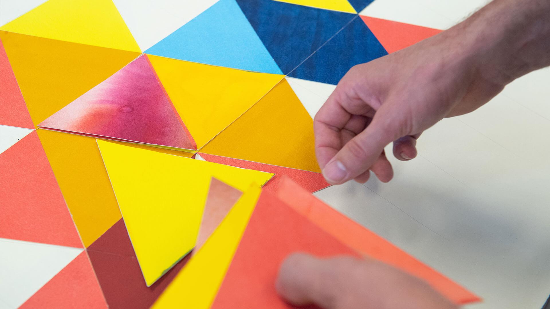 A hand lays down multicolored triangles.