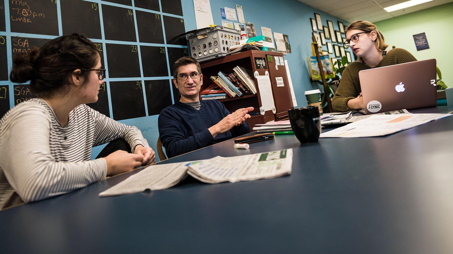 three people at a desk reviewing newspapers