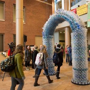 Students walk under arch of recycled bottles