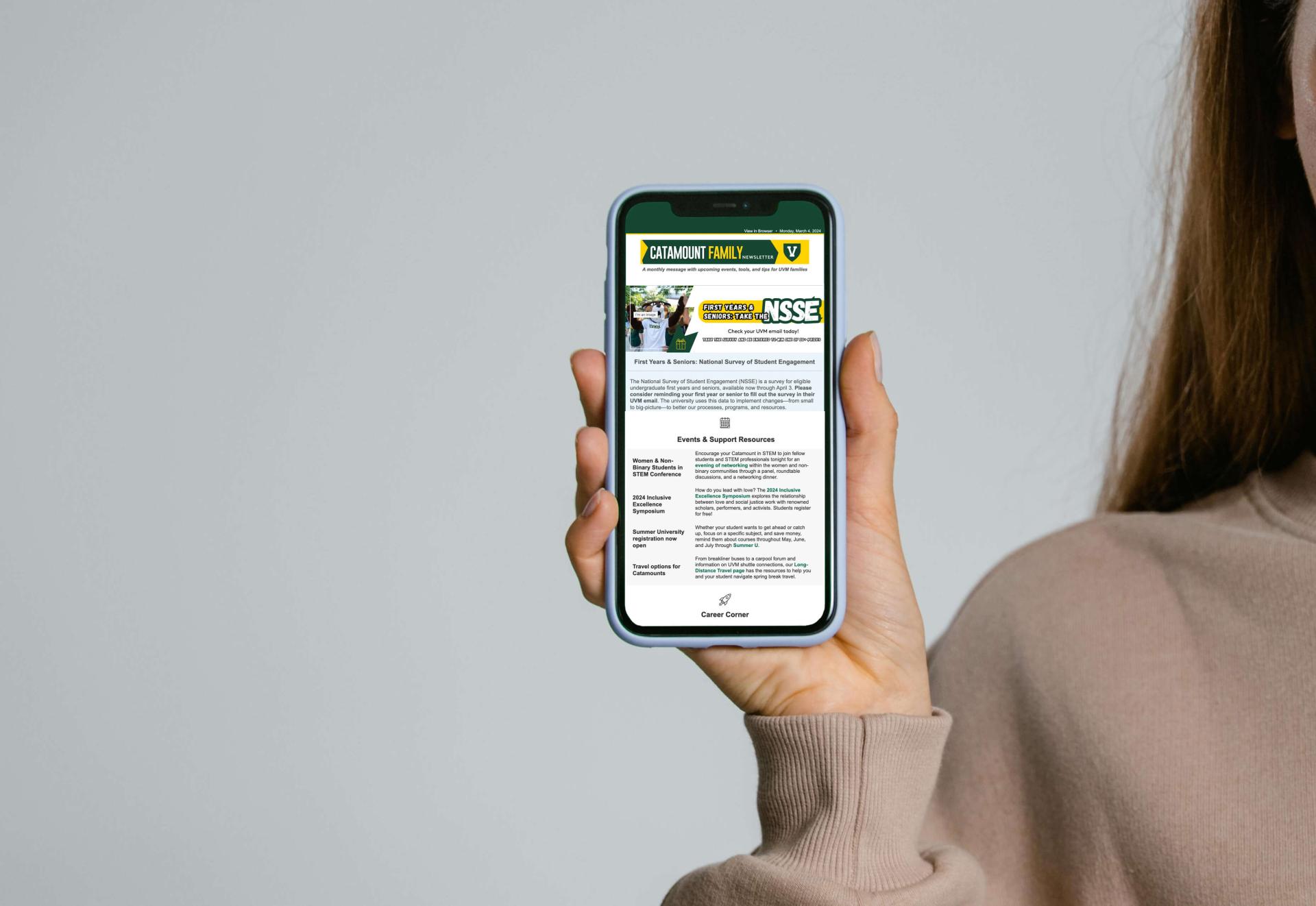 A hand holding an iPhone, it's screen displaying an issue of the Catamount Family Newsletter