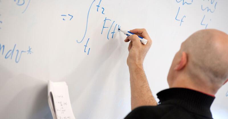 A professor solves an equation on a whiteboard