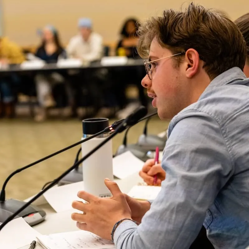 A student speaking into a microphone at a meeting.
