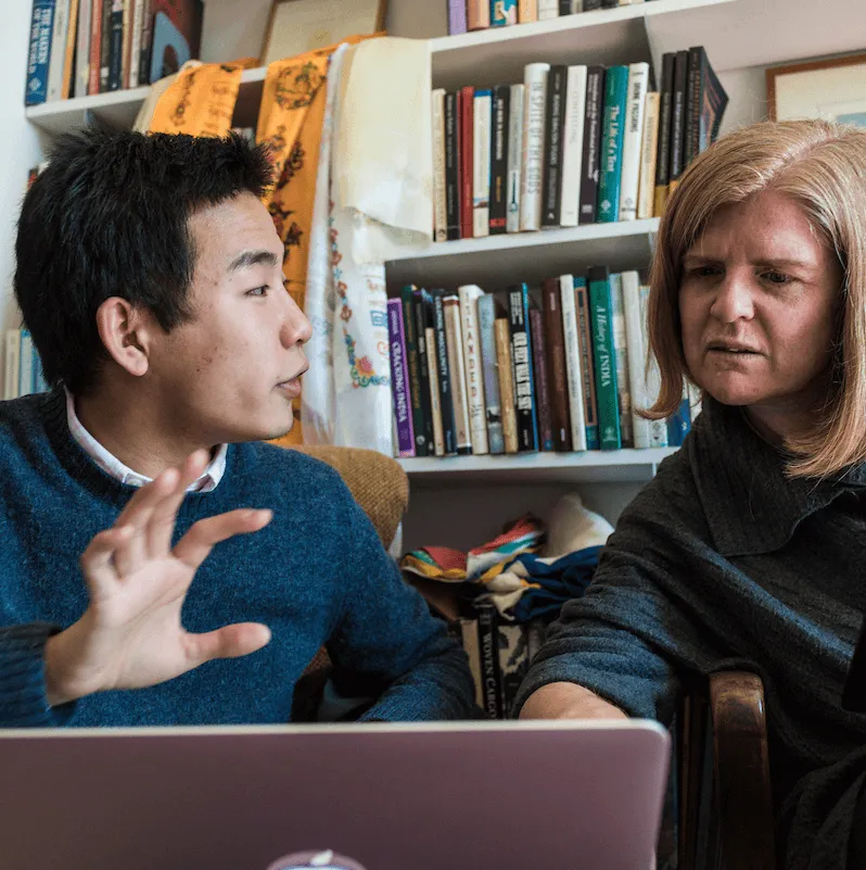 Student and professor chat and look at a laptop screen
