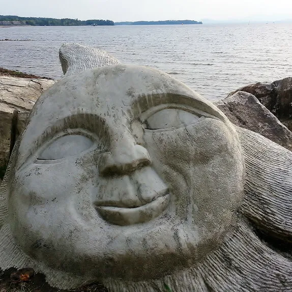 Smiling sun face carved into stone on shore of a lake