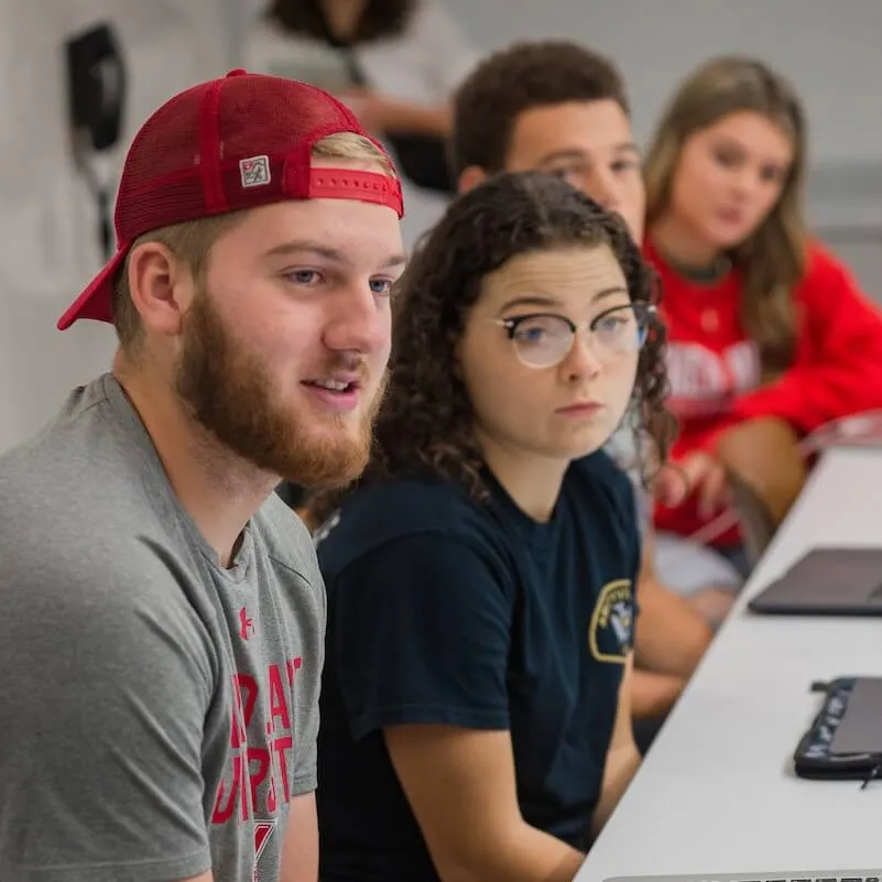 Students sit in a row at a table during a class discussion.