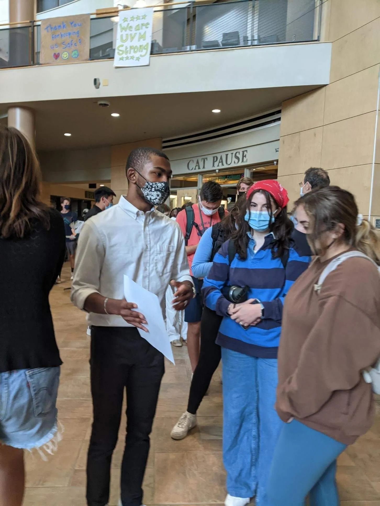Three students stand wearing face masks in a crowded university building.