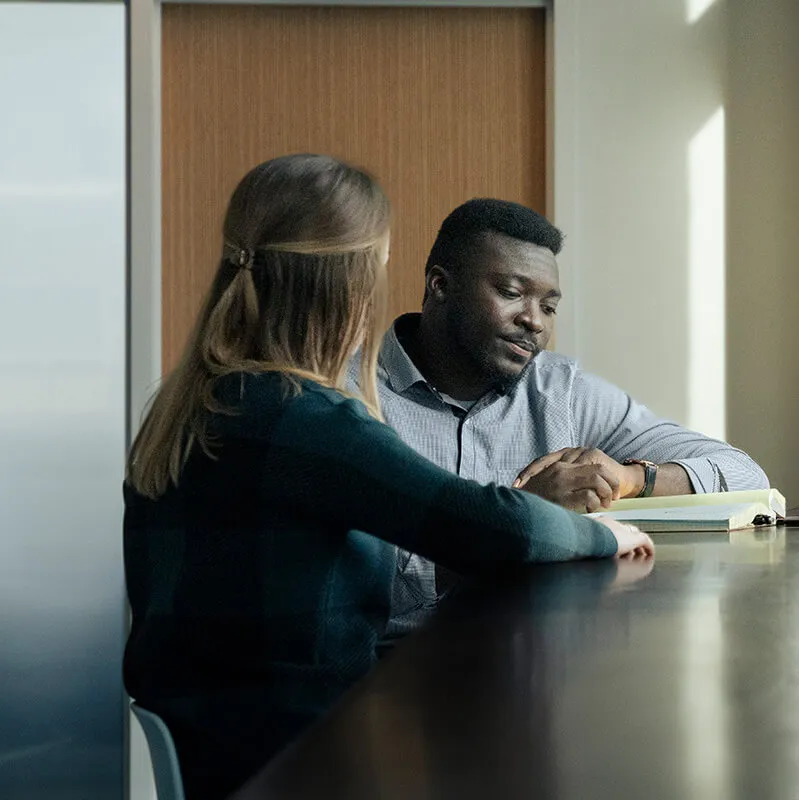 Two person sitting at a table in an office, engaged in a discussion