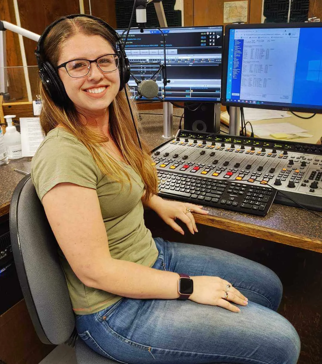 A young woman smiles while wearing headphones in a production booth.