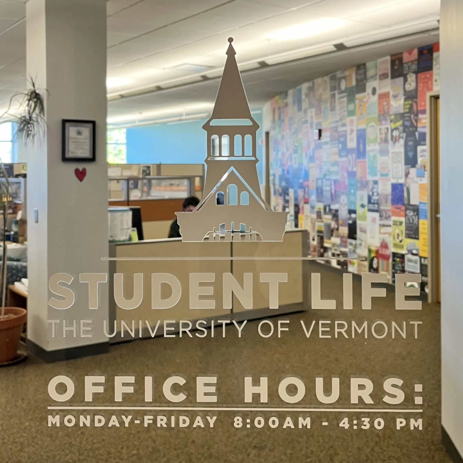 Glass door outside of the student life office with the UVM Logo and the "Student Life" logo alongside the office hours of operation