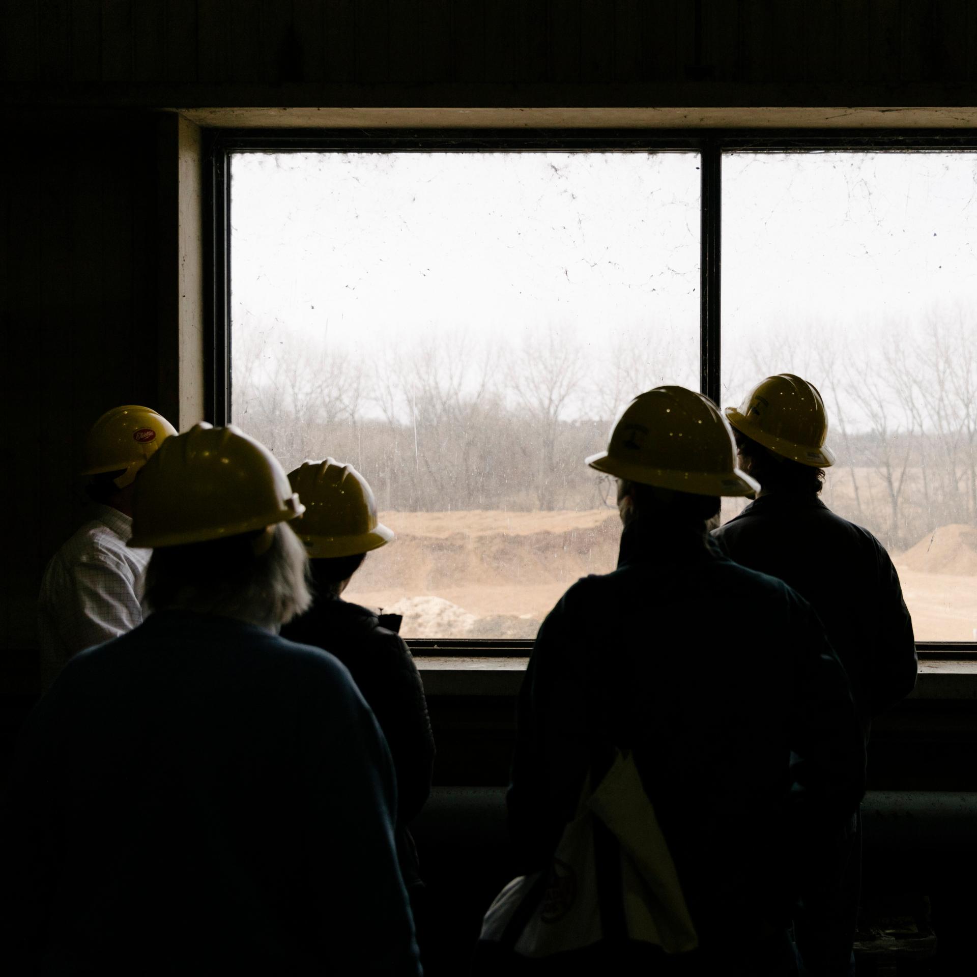 Students in an electricity facility with hard hats listening to tour leader. 