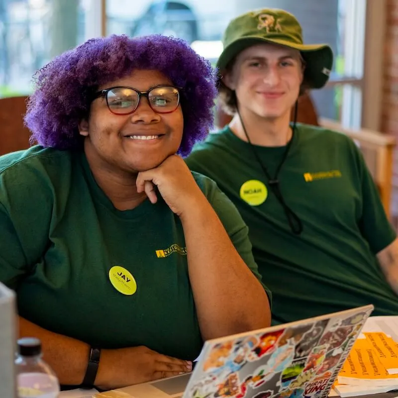 Two students smiling in green UVM uniform t-shirts.