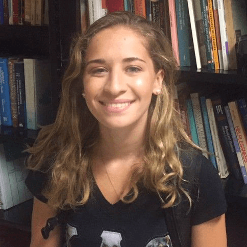 A smiling student, against a group of booklined shelves