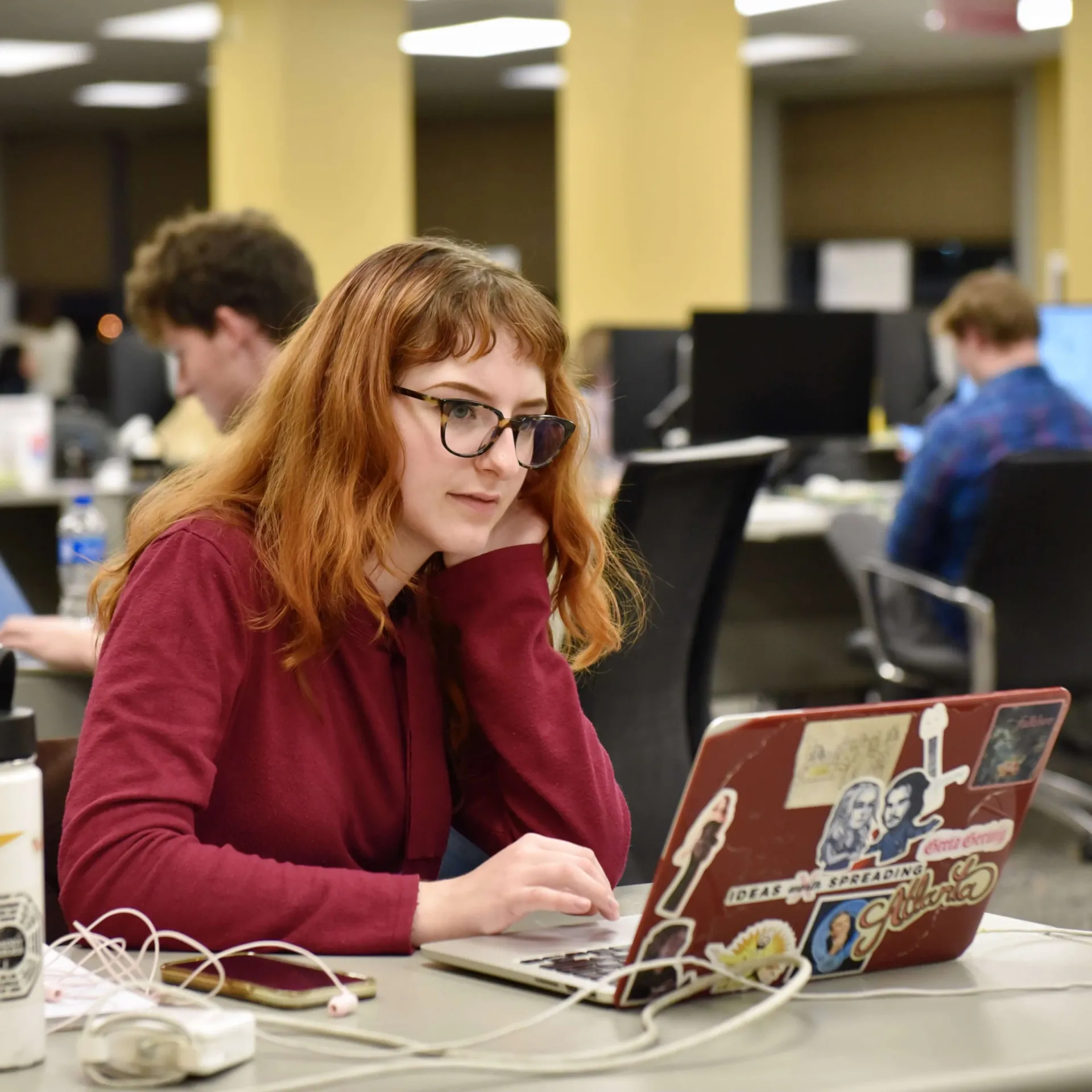 A young woman with bright red hair works on her laptop.