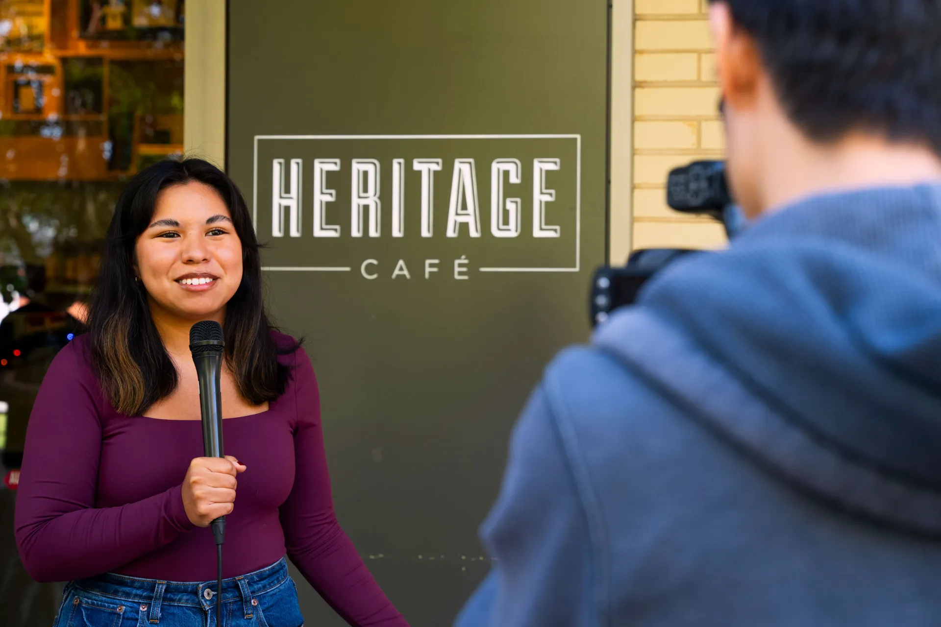 Students work together to film a news segment in front of Heritage cafe.