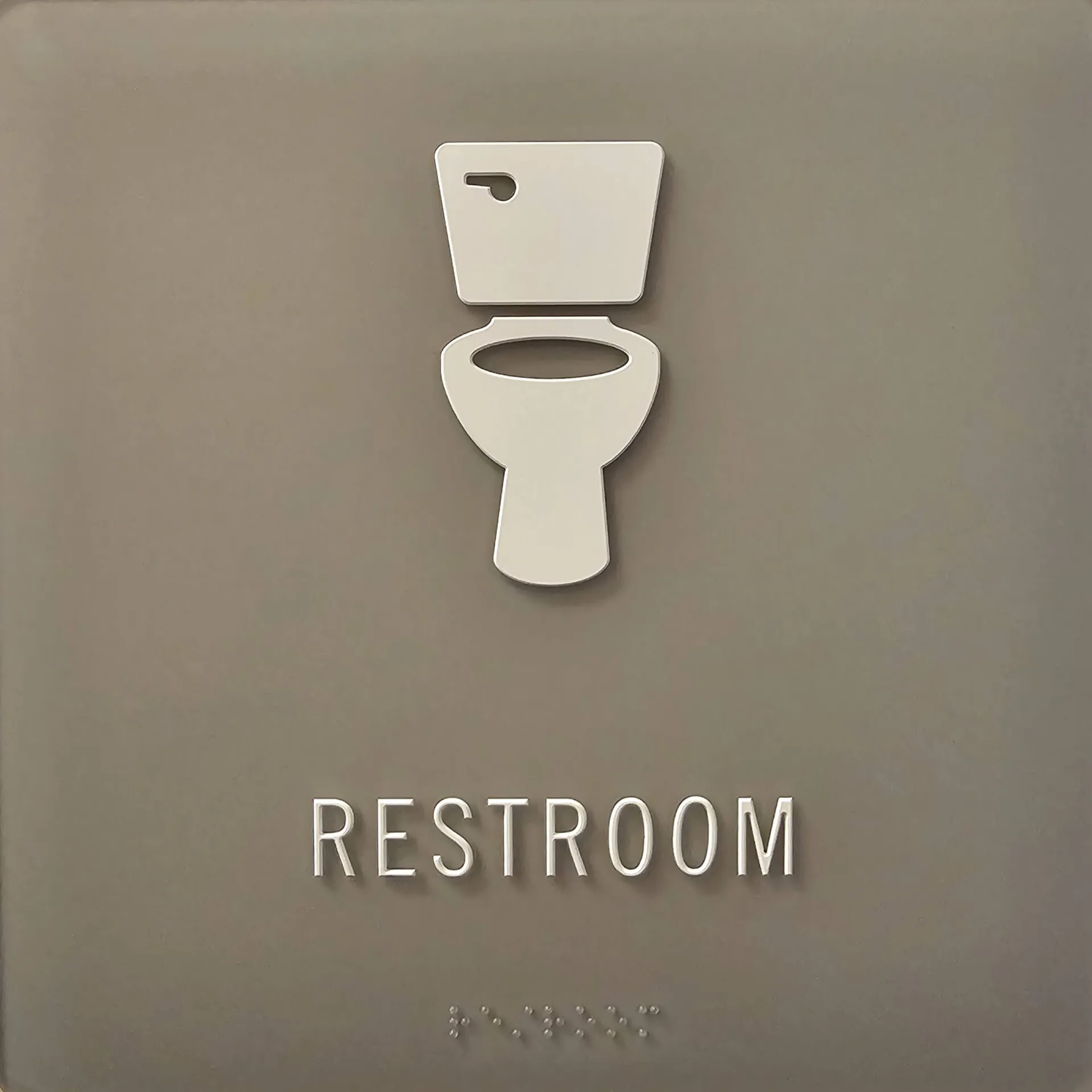 A grey restroom sign with a icon of a toilet, the word "restroom" written in English and embossed in braille. 