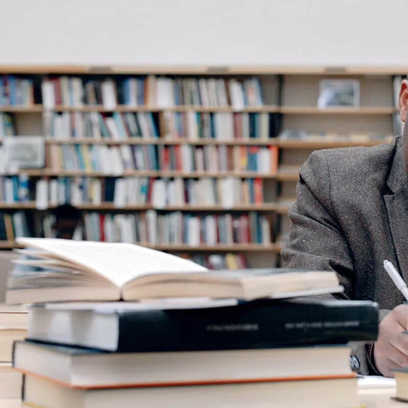 person at a library desk taking notes with books