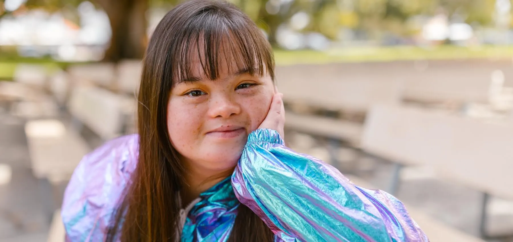 Young woman with Down syndrome, sitting on a bench outdoors, smiling at the camera