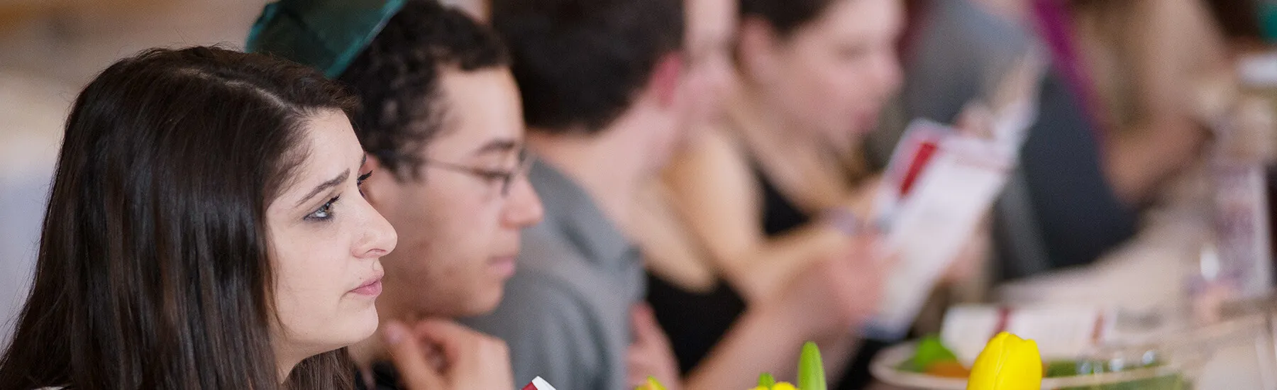 A woman with long hair sitting at a table, surrounded by a group of people