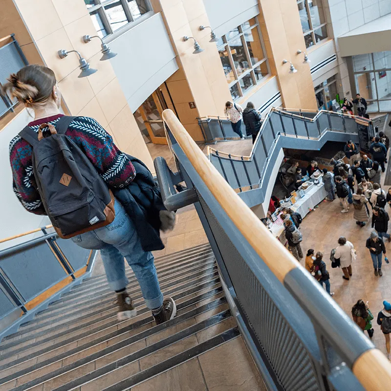Student walking down stairs in Davis Center, crowd of people seen below in the Davis atrium. 