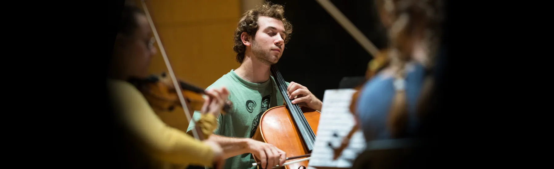 Musicians playing the cello and violin surrounded by a group of people 