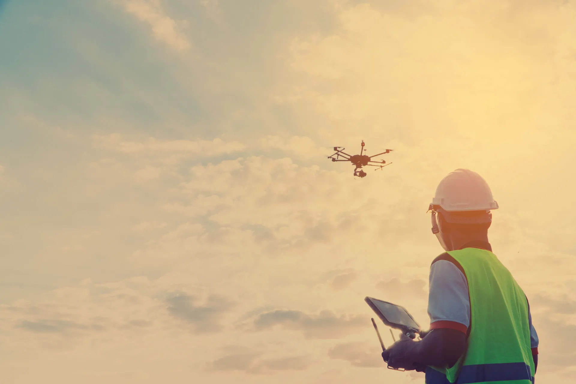 Man in hardhat and safety vest flies a drone.