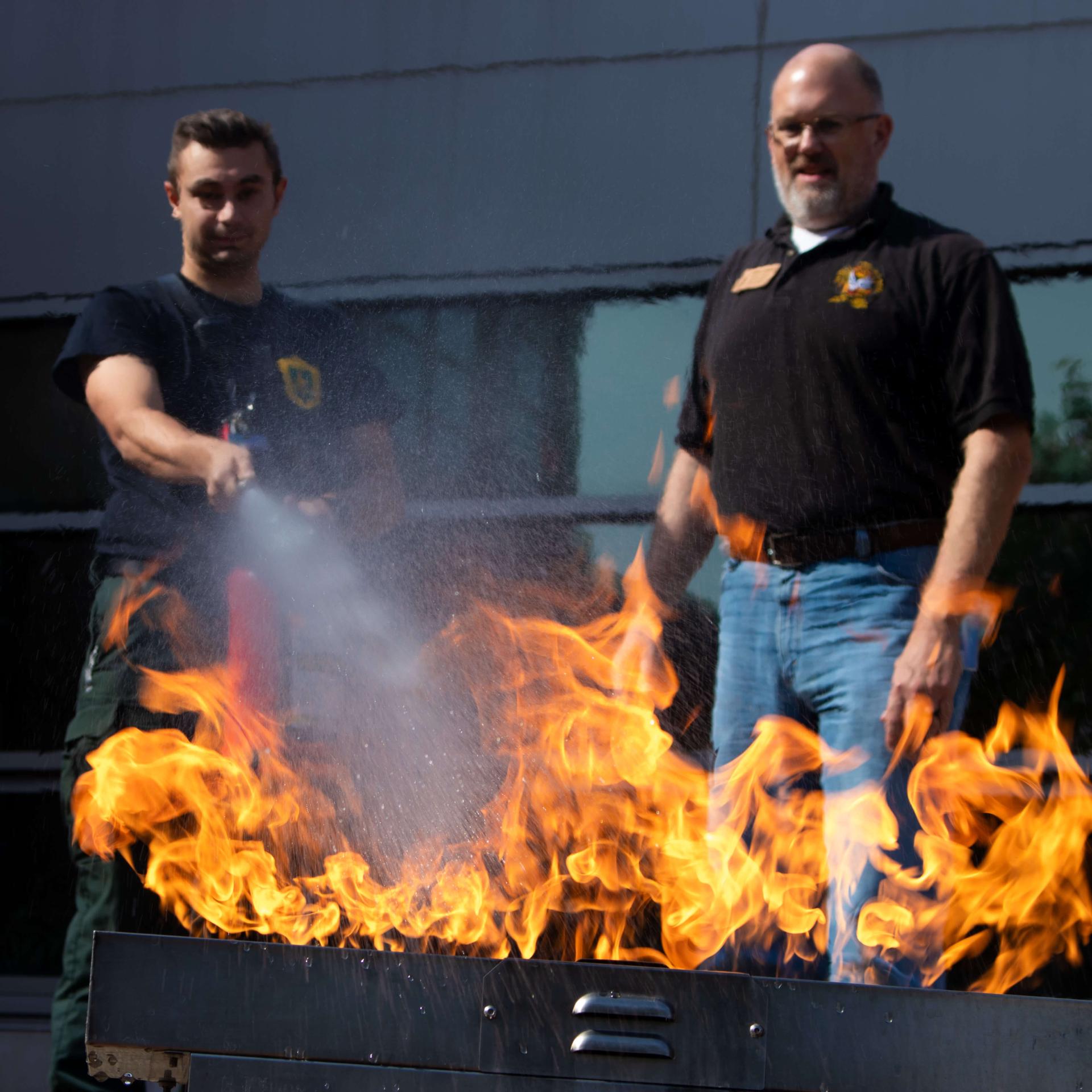 Member of UVM Rescue spraying fire extinguisher with Fire Marshal standing by.