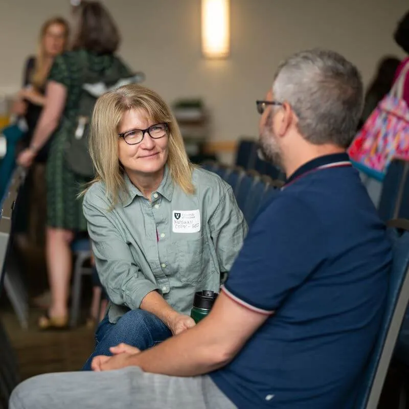UVM faculty sit in a row of chair having a conversation while another group of employees gather behind them to talk