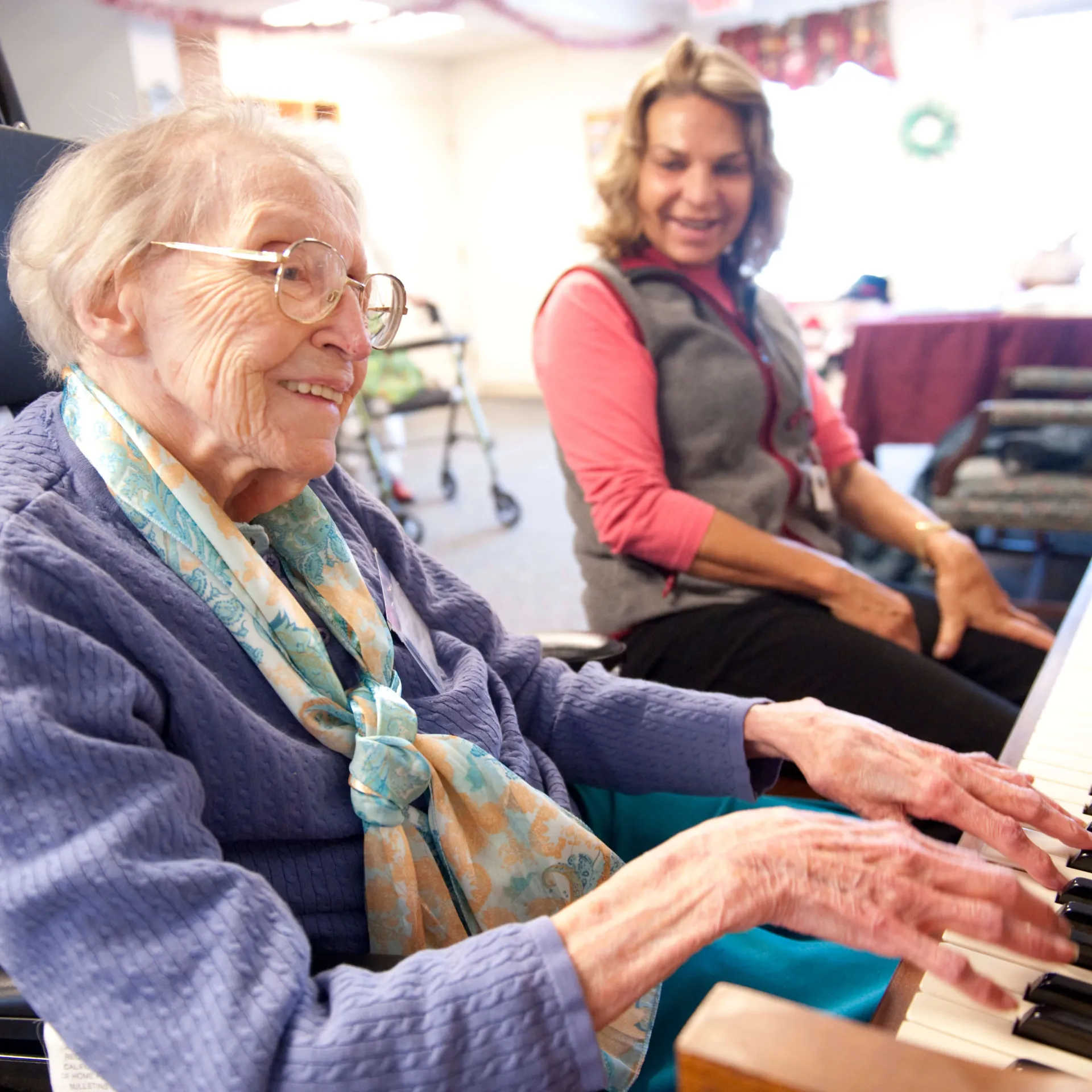 A medical staff member listening to an elderly person play the piano. 