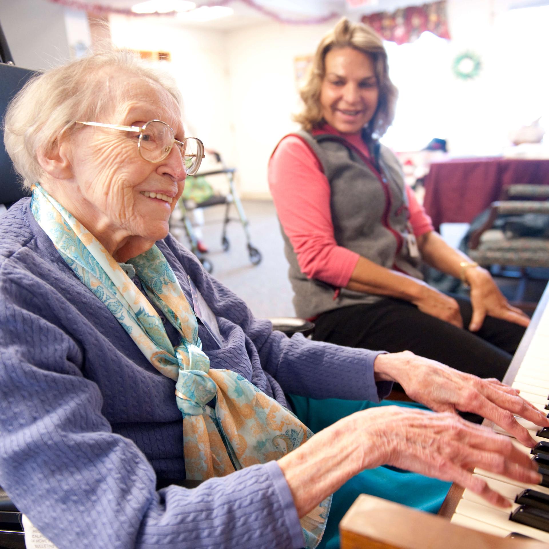 A medical staff member listening to an elderly person play the piano. 