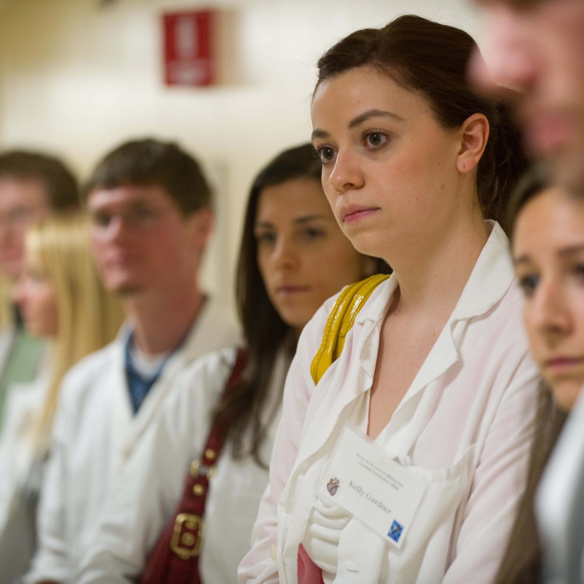 Femme presenting person in a group of students listening to a speaker. 