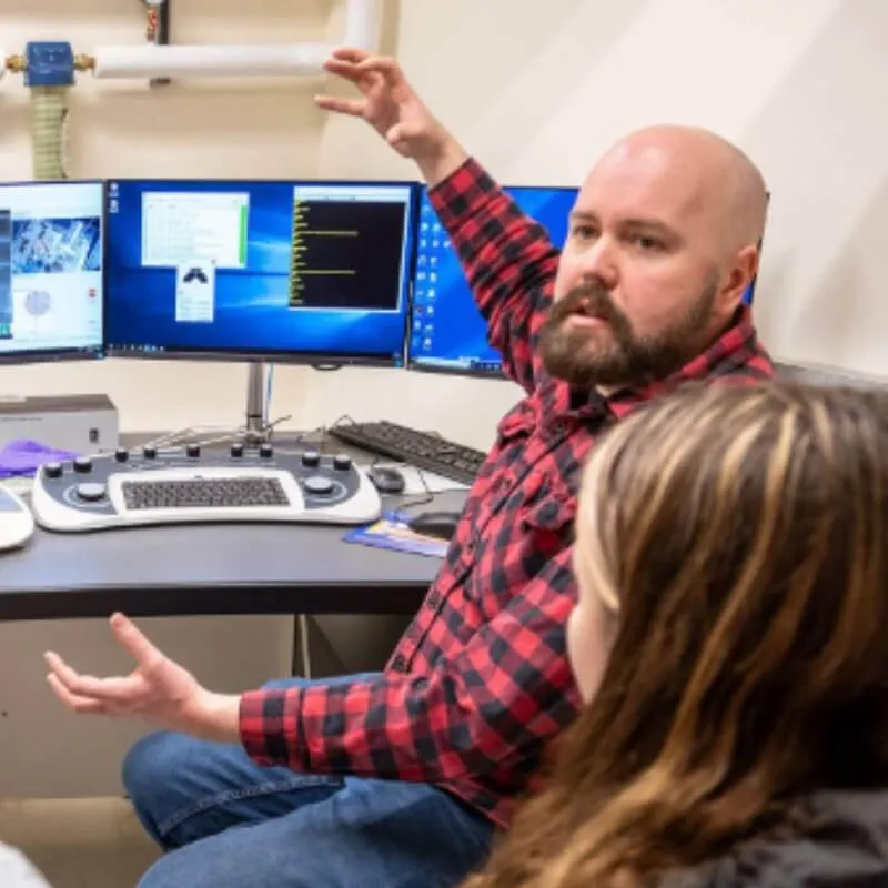 A person sitting in front of a computer using arms and hands to explain something to others.