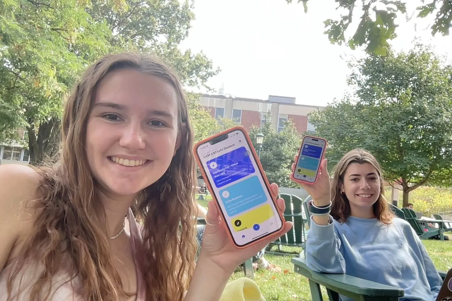 Two students sitting outside holding up iPhones with the CatSafe App visible