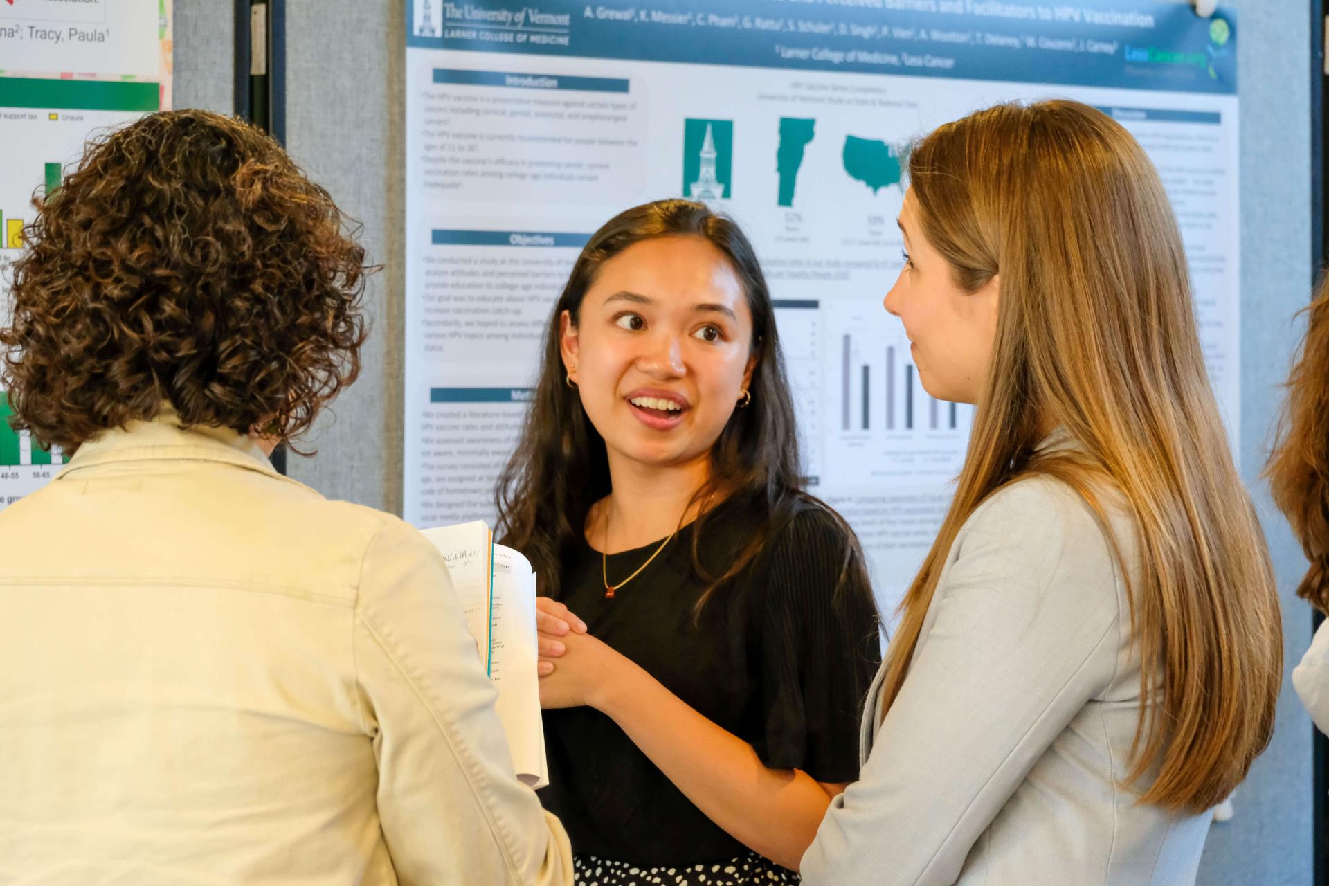 Three femme presenting people discussing a student poster project. 