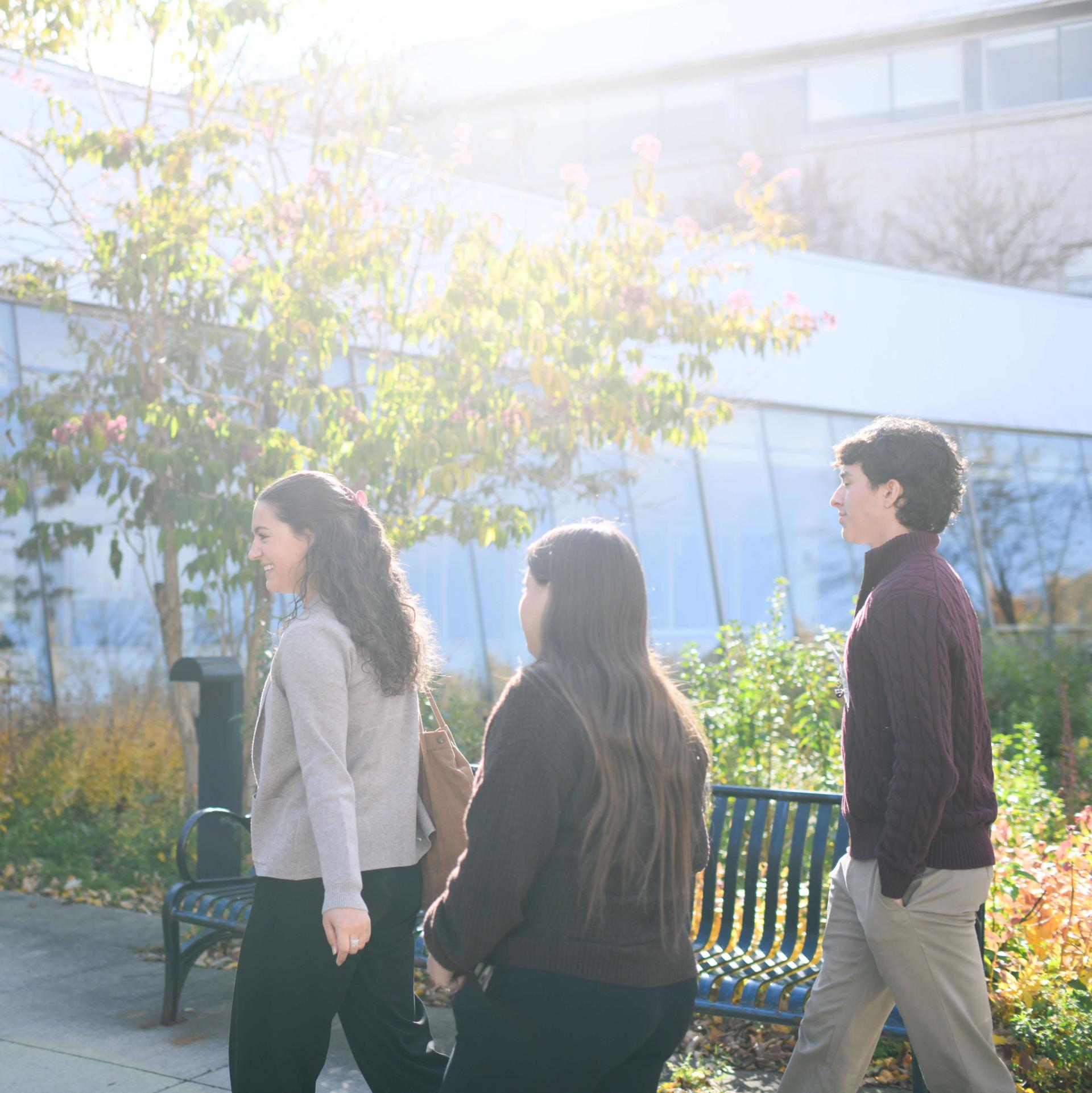Three students, two femme presenting, and one masculine presenting, walking into Larner College of Medicine.