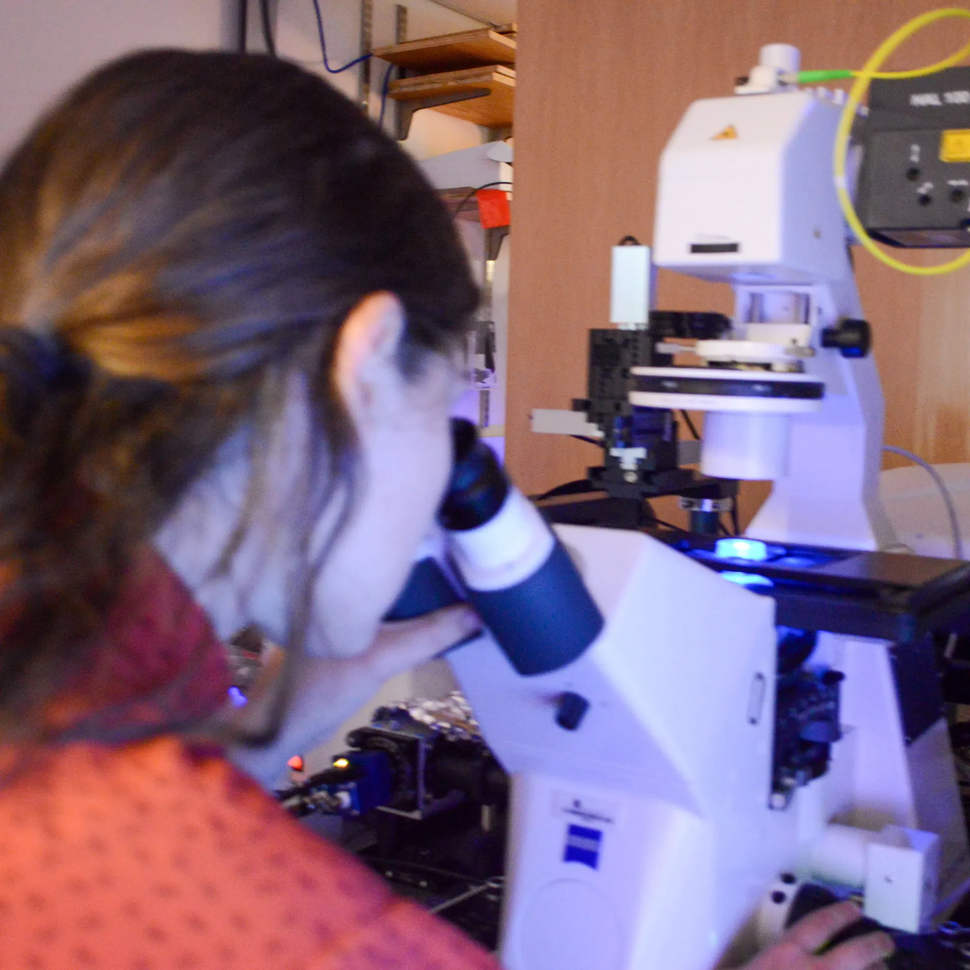 A femme presenting student analyzing samples under a microscope.