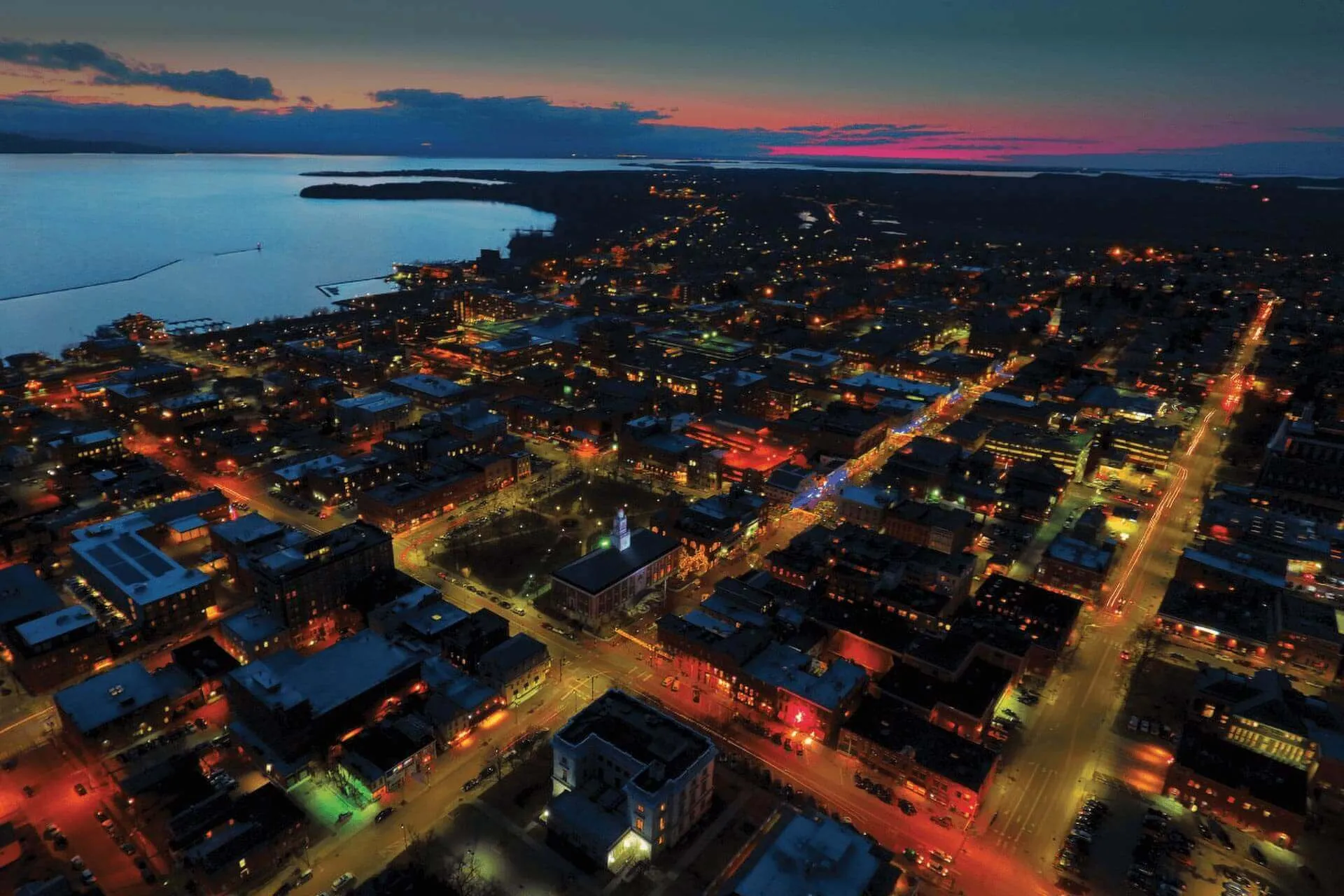 Aerial view of Burlington and the UVM Campus at sunset accented by colorful lights and the lake.