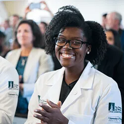 A smiling black, female medical student gets her white coat.
