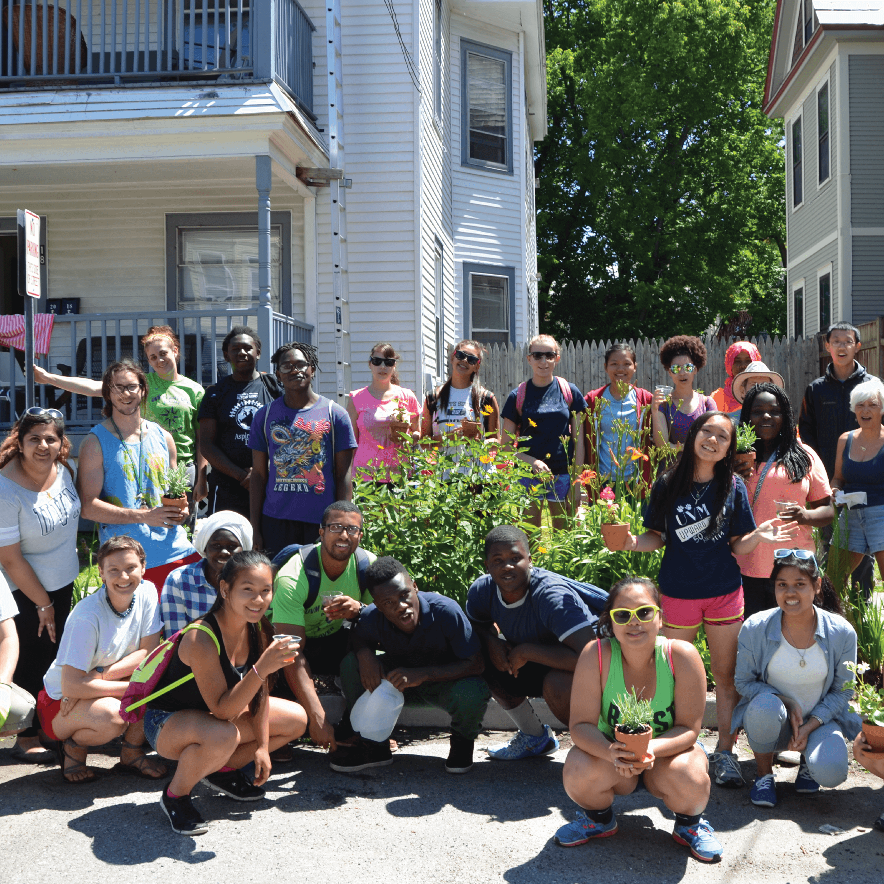 Multi-racial, multi-generational group of people pose in front of a community garden.